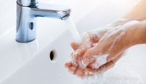 Woman uses soap to washing her hands under the sink faucet.
